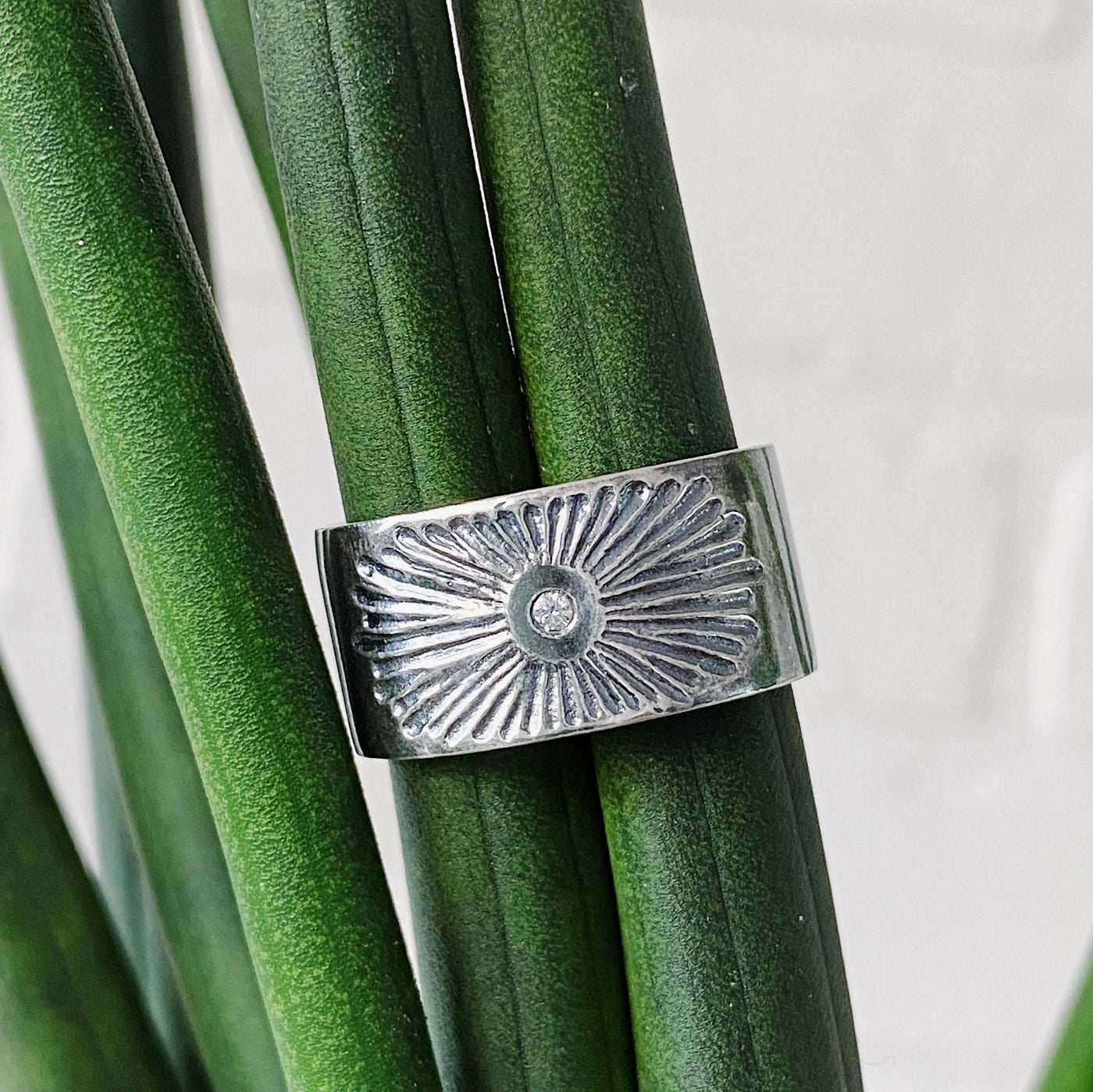 Oxidized silver wide band with single diamond and a carved sunburst design in natural light by Corey Egan