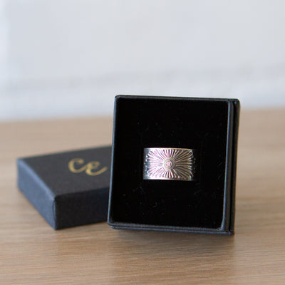 Oxidized silver wide band with single diamond and a carved sunburst design in a ring box by Corey Egan