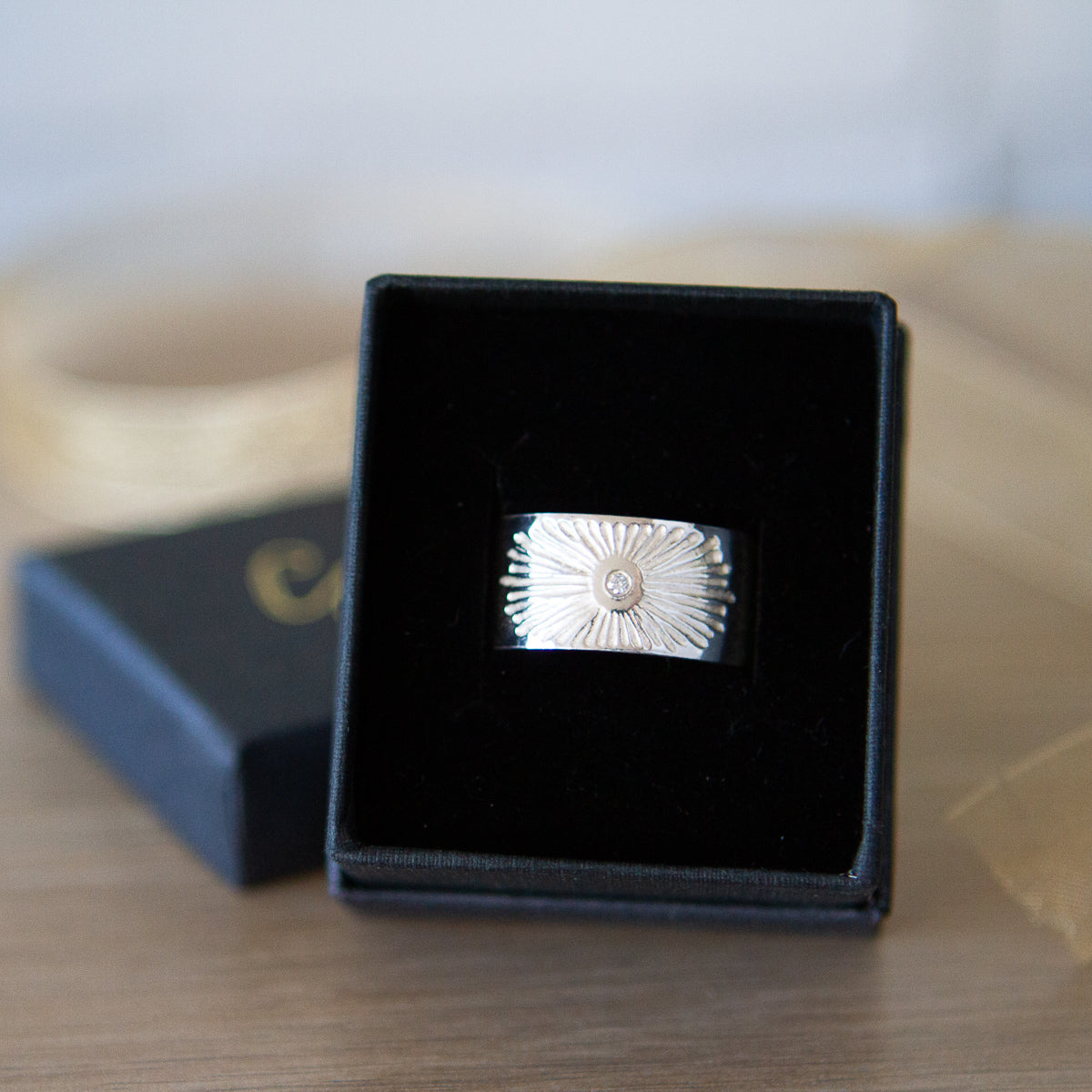 Sterling silver wide band with single diamond and a carved sunburst design in a ring box by Corey Egan