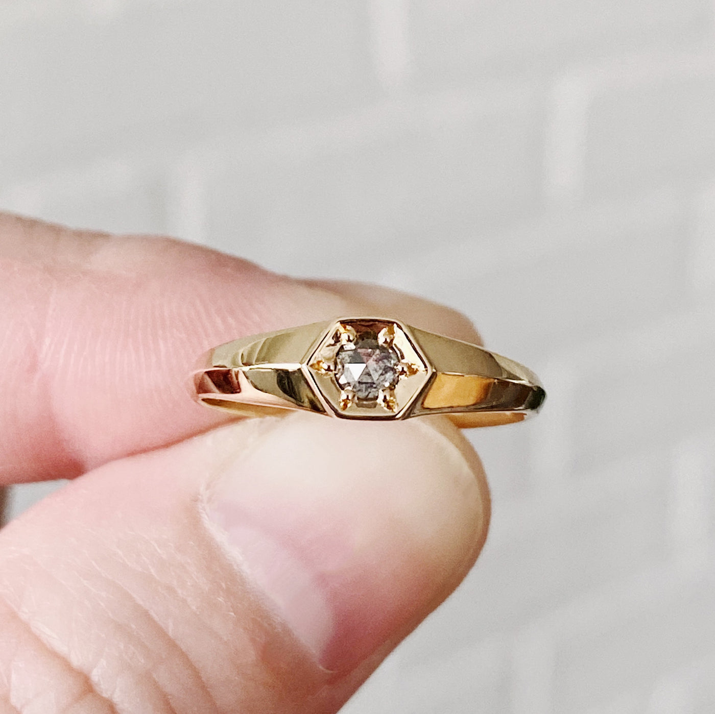 Yellow gold signet ring with bead set rose cut salt and pepper diamond held between two fingers
