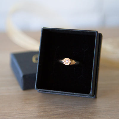 Low profile gold signet ring with hexagon top and a single white diamond set within a six pointed star setting in a gift box