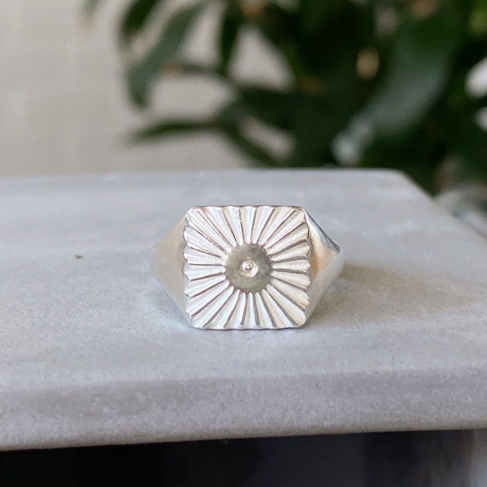 Large silver square signet ring with a carved sunburst pattern and single silver bead in the center