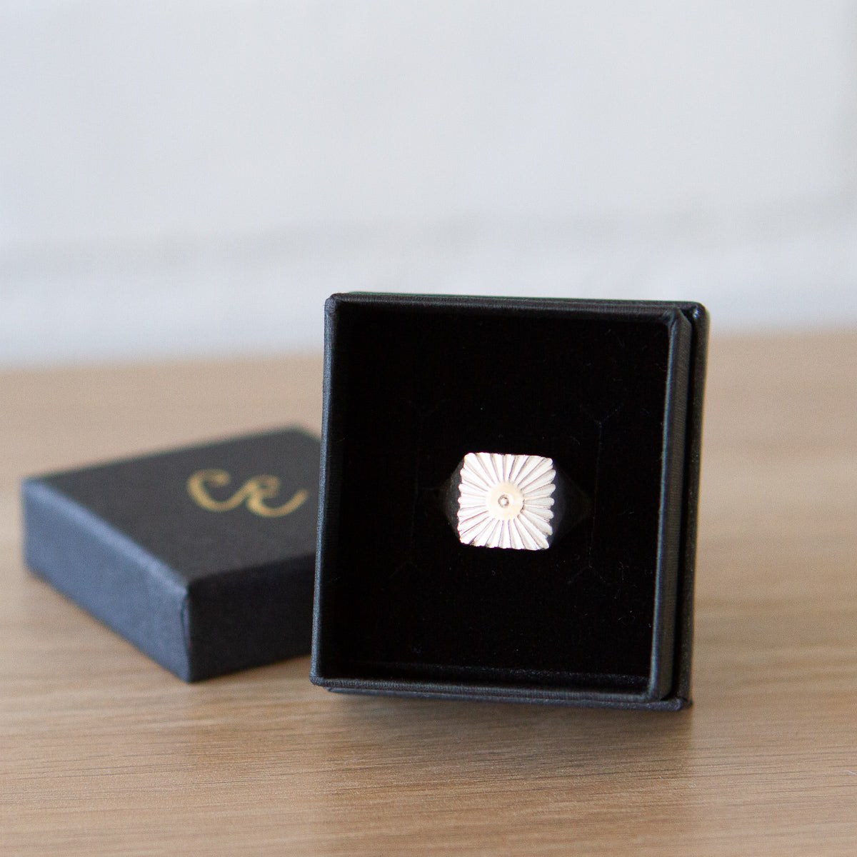Large silver square signet ring with a carved sunburst pattern and single silver bead in the center in a gift box