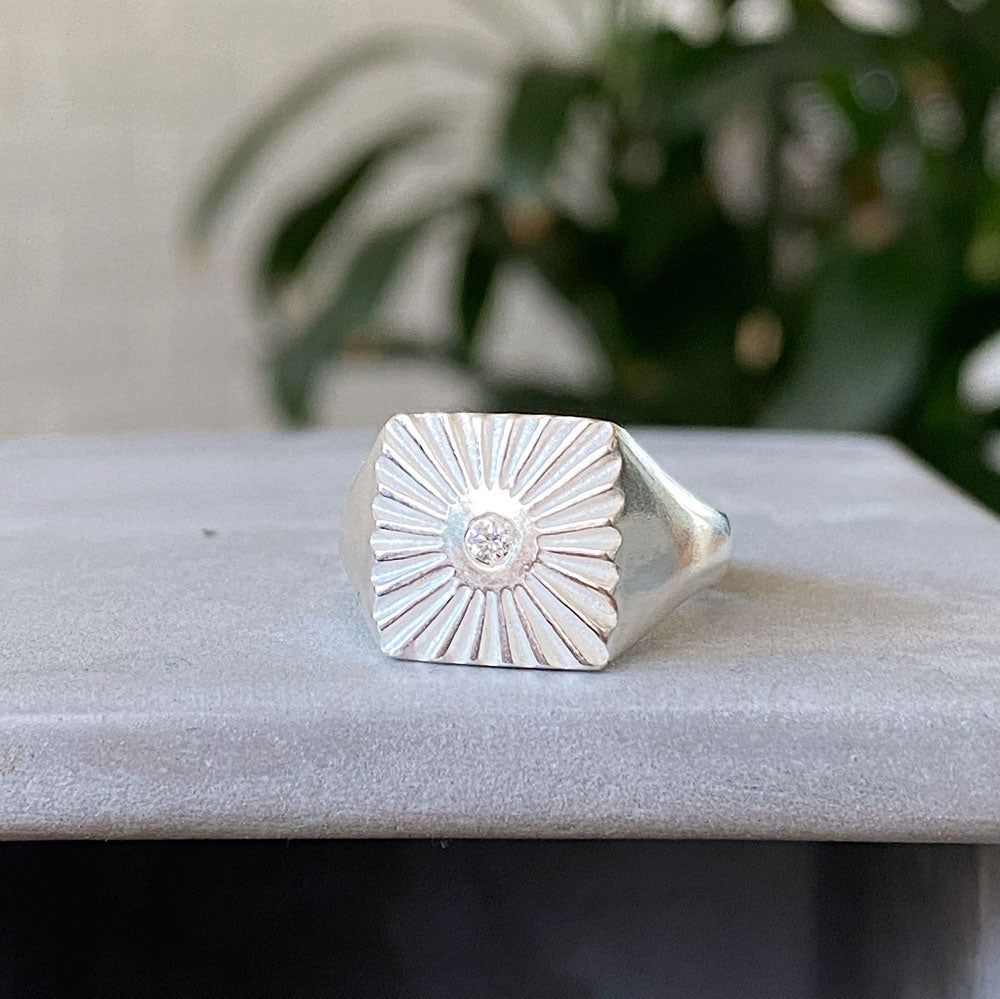 Side view of Large silver square signet ring with a carved sunburst pattern and diamond center
