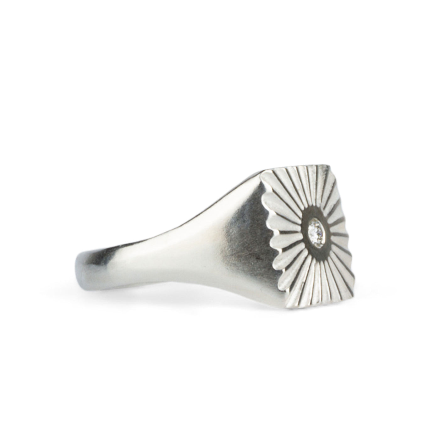 Side view of large silver square signet ring with a carved sunburst pattern and diamond center on a white background