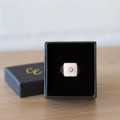 Large silver square signet ring with a carved sunburst pattern and diamond center in a gift box