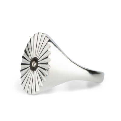 Side view of Large silver oval signet ring with a carved sunburst pattern and a silver bead center on a white backtround