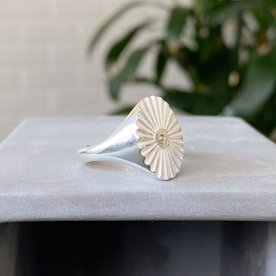 Side view of large silver oval signet ring with a carved sunburst pattern and a silver bead center