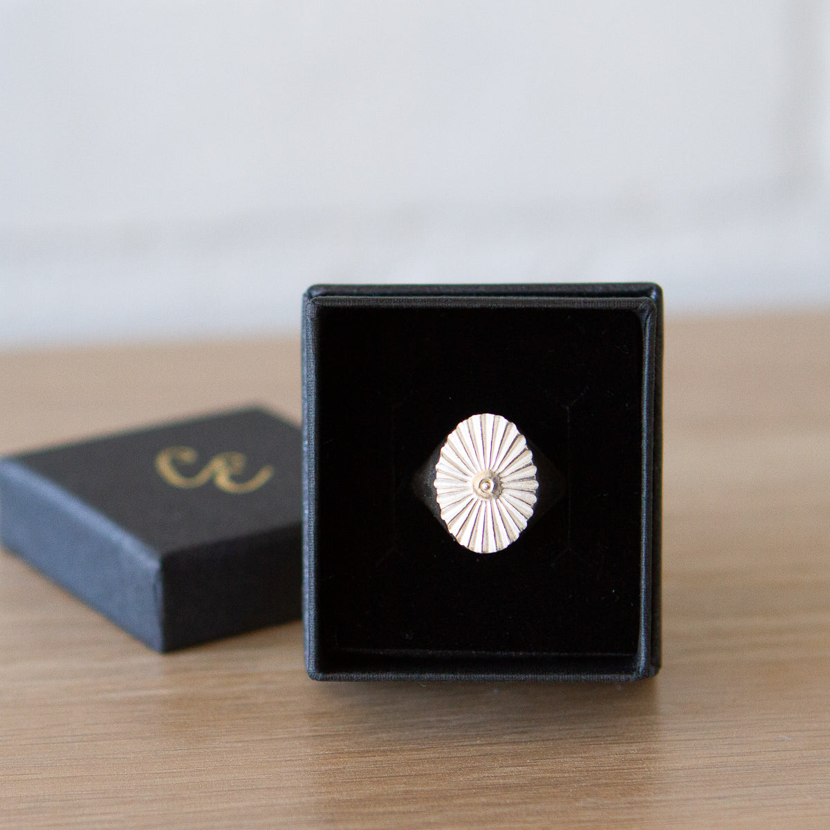 Large silver oval signet ring with a carved sunburst pattern and a silver bead center in a gift box