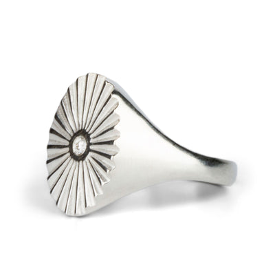 Side view of Large silver oval signet ring with a carved sunburst pattern and diamond center on a white background