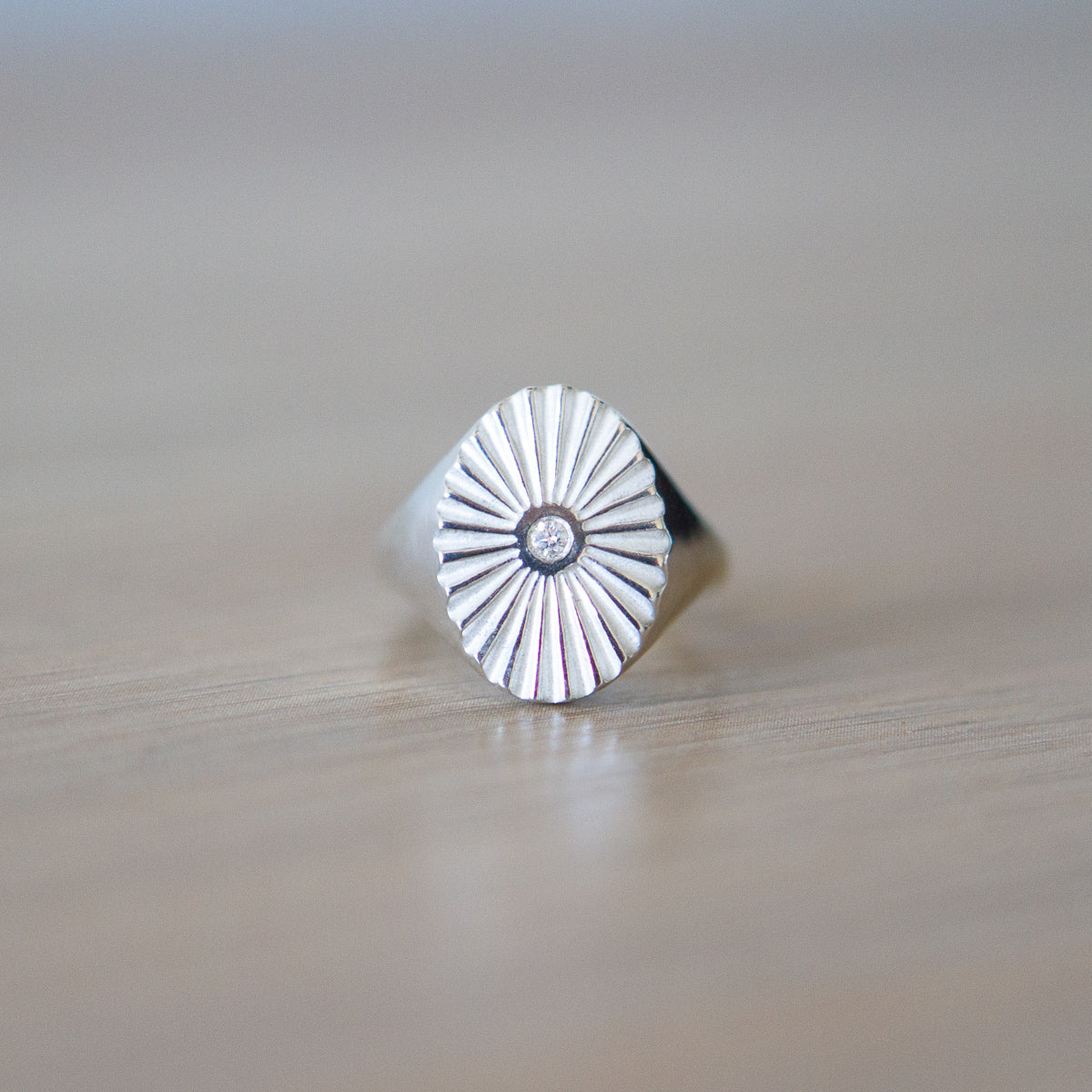 Large silver oval signet ring with a carved sunburst pattern and diamond center