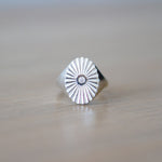 Large silver oval signet ring with a carved sunburst pattern and diamond center