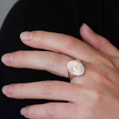 Large silver oval signet ring with a carved sunburst pattern and diamond center on a hand
