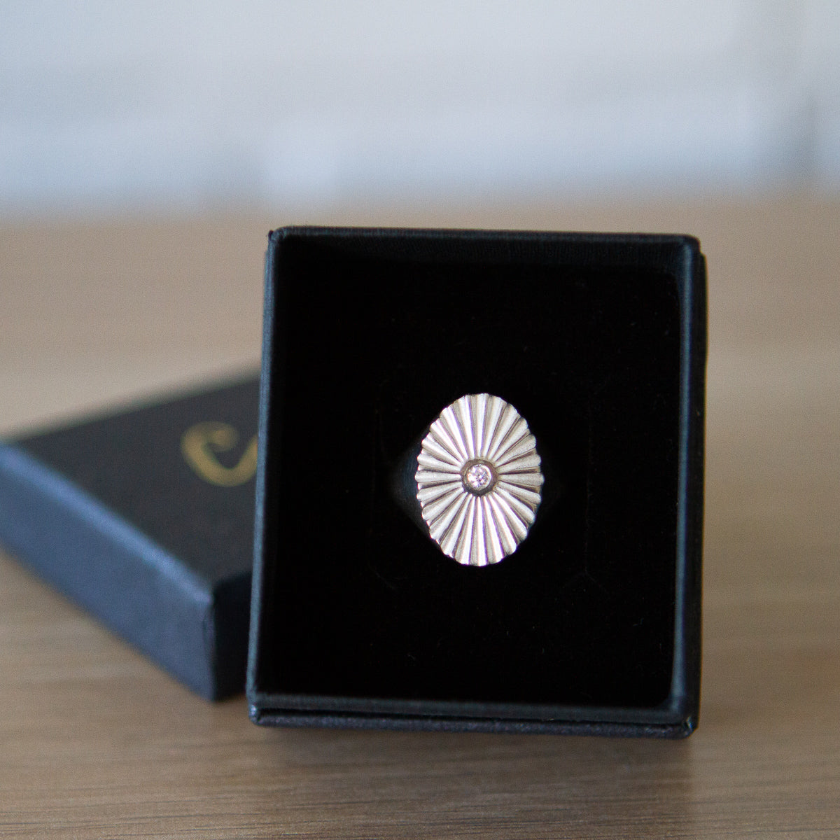 Large silver oval signet ring with a carved sunburst pattern and diamond center in a gift box