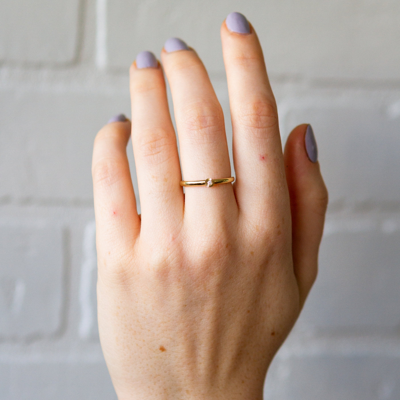14k Yellow Gold small aurora stacking ring with a 1.5mm center diamond and engraved border on a hand