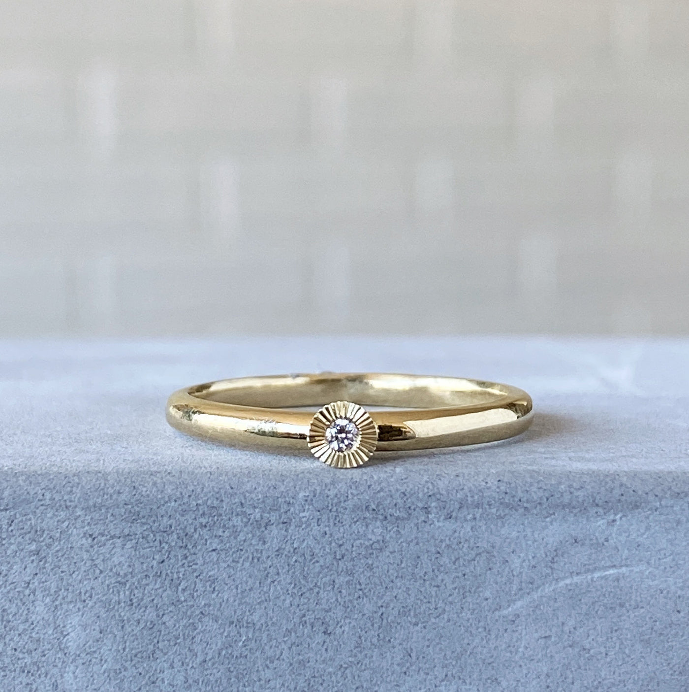 14k yellow gold small aurora stacking ring with a 1.5mm center diamond and engraved border on concrete