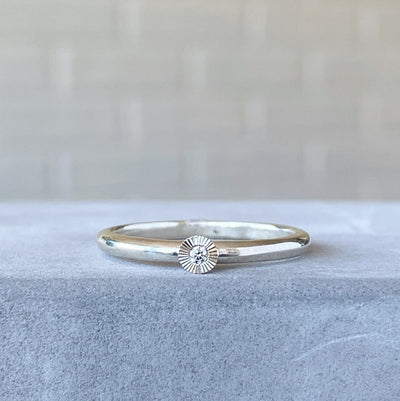 sterling silver small aurora stacking ring with a 1.5mm center diamond and engraved border on concrete