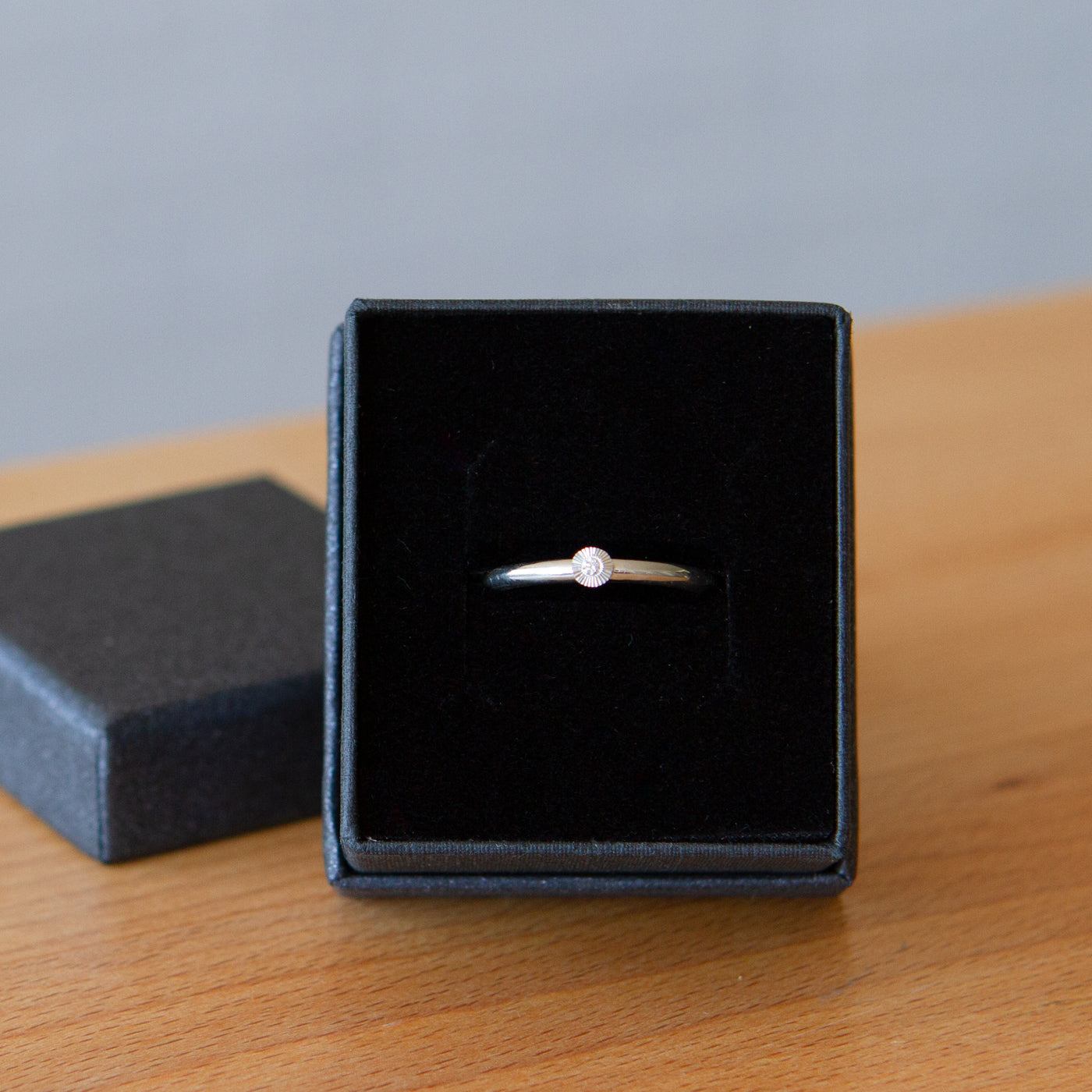sterling silver small aurora stacking ring with a 1.5mm center diamond and engraved border in a ring box
