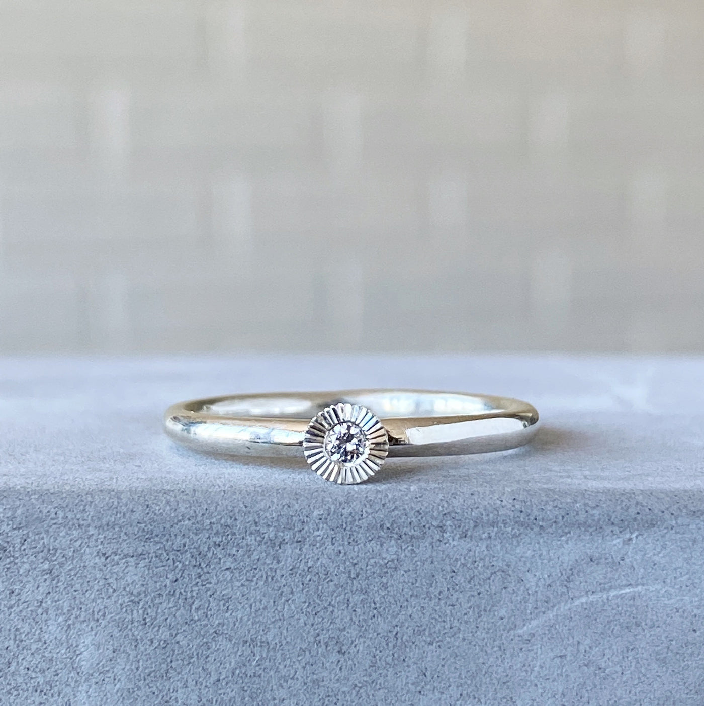 sterling silver small aurora stacking ring with a 2mm center diamond and engraved border on concrete