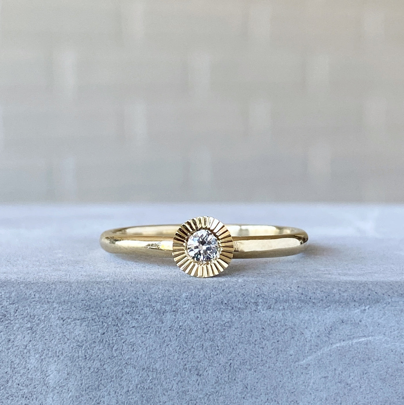 14k yellow gold large aurora stacking ring with a 3mm center diamond and engraved border resting on concrete
