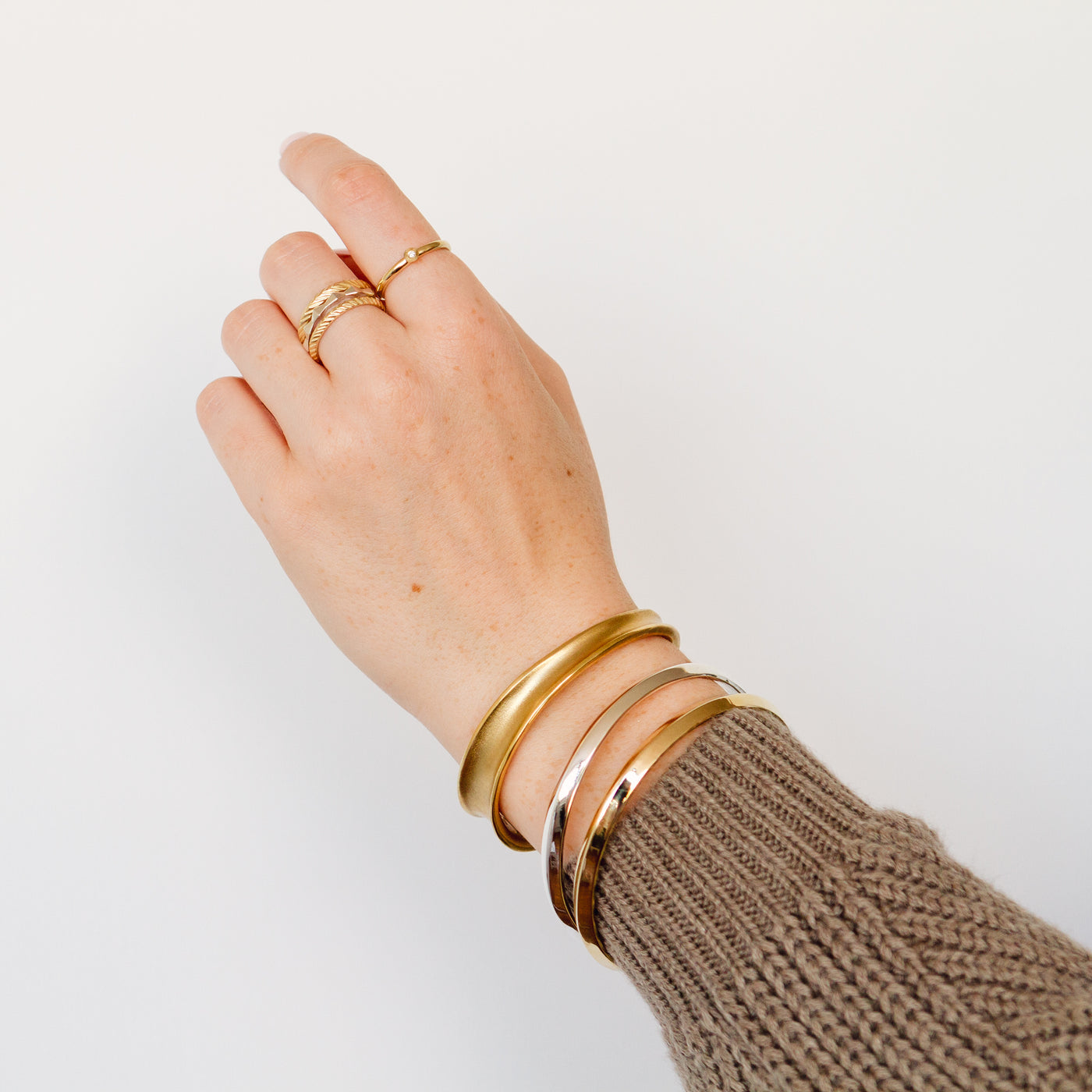A hand wearing gold rings and the bronze ebb cuff on her wrist with a silver and bronze aura bangle