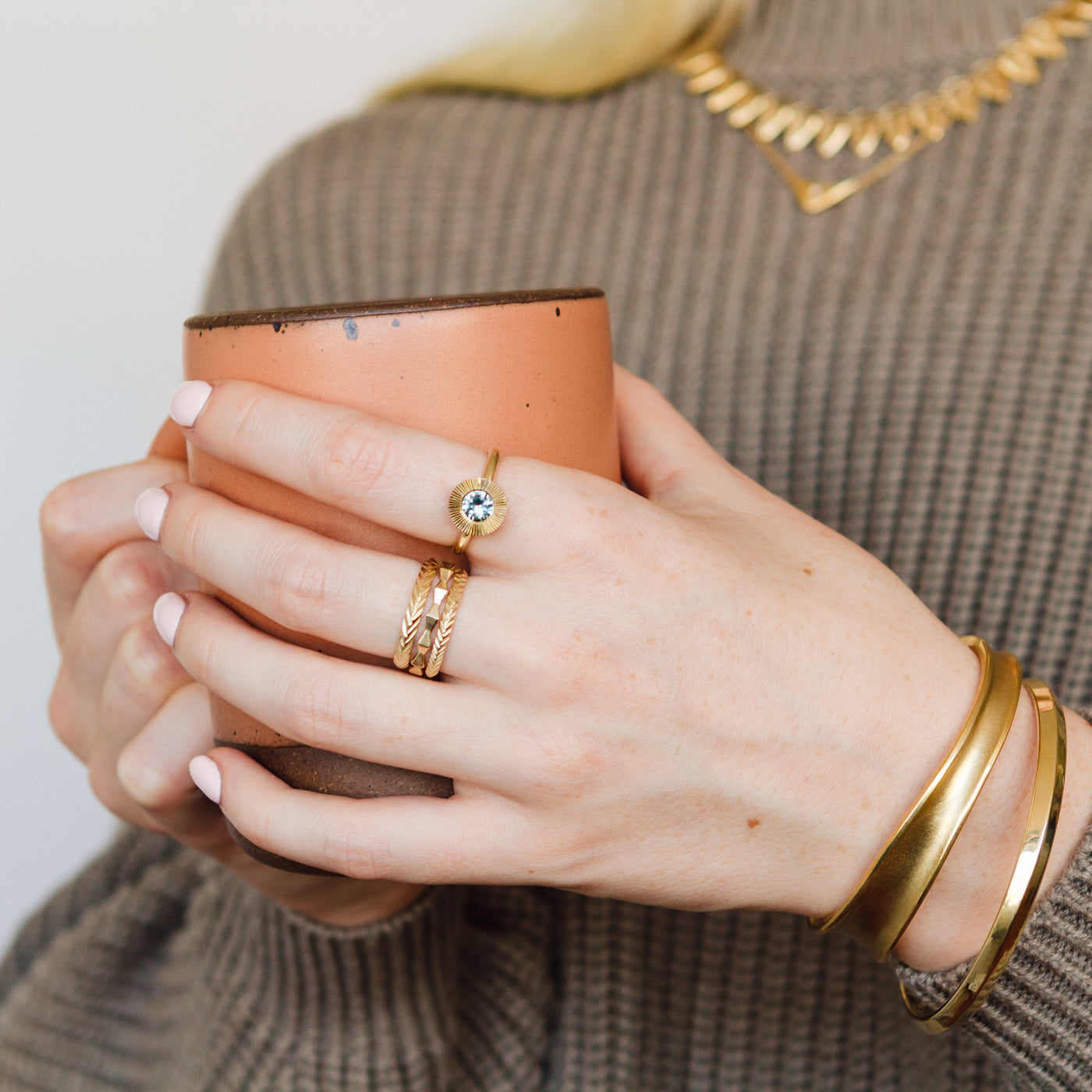  hand holding a mug with the bronze Ebb cuff and a bronze aura bangle on her wrist