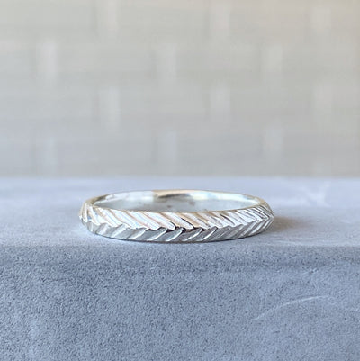 sterling silver stackable herringbone carved band 3mm width resting on concrete