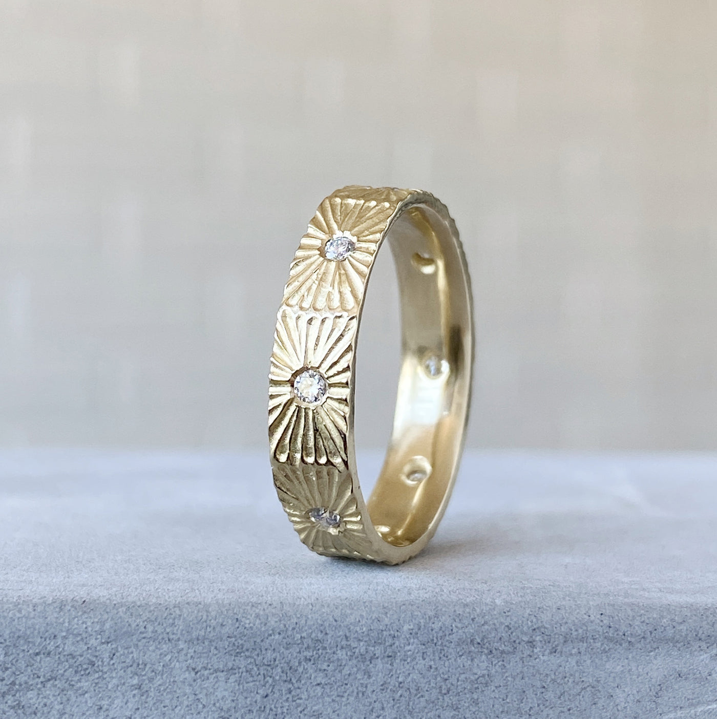 Nova sunburst eternity band with 8 flush set diamonds and carved texture around the outside in 14k yellow gold on concrete