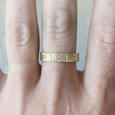 Nova sunburst eternity band with 8 flush set diamonds and carved texture around the outside in 14k yellow gold on a hand