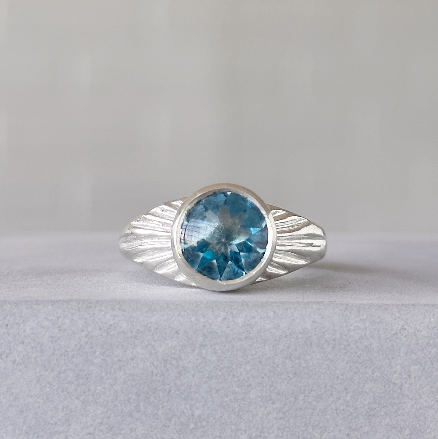 Blue Topaz Silver Sunburst Ring sitting in front of a white wall, front angle