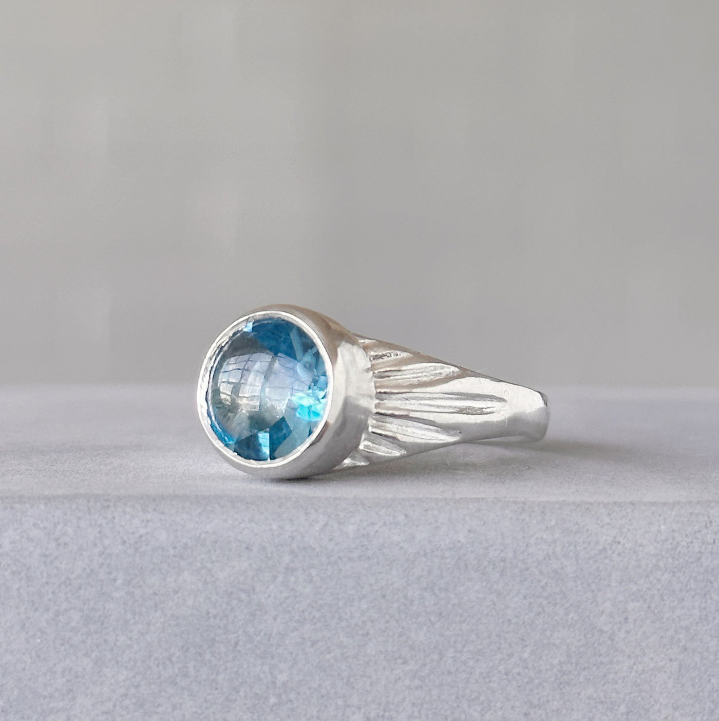 Blue Topaz Silver Sunburst Ring sitting in front of a white wall, side angle
