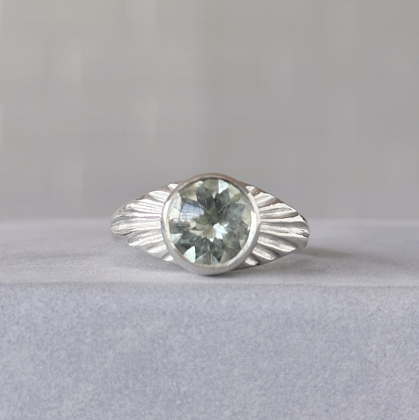Green Amethyst Silver Sunburst Ring sitting in front of a white wall, front angle