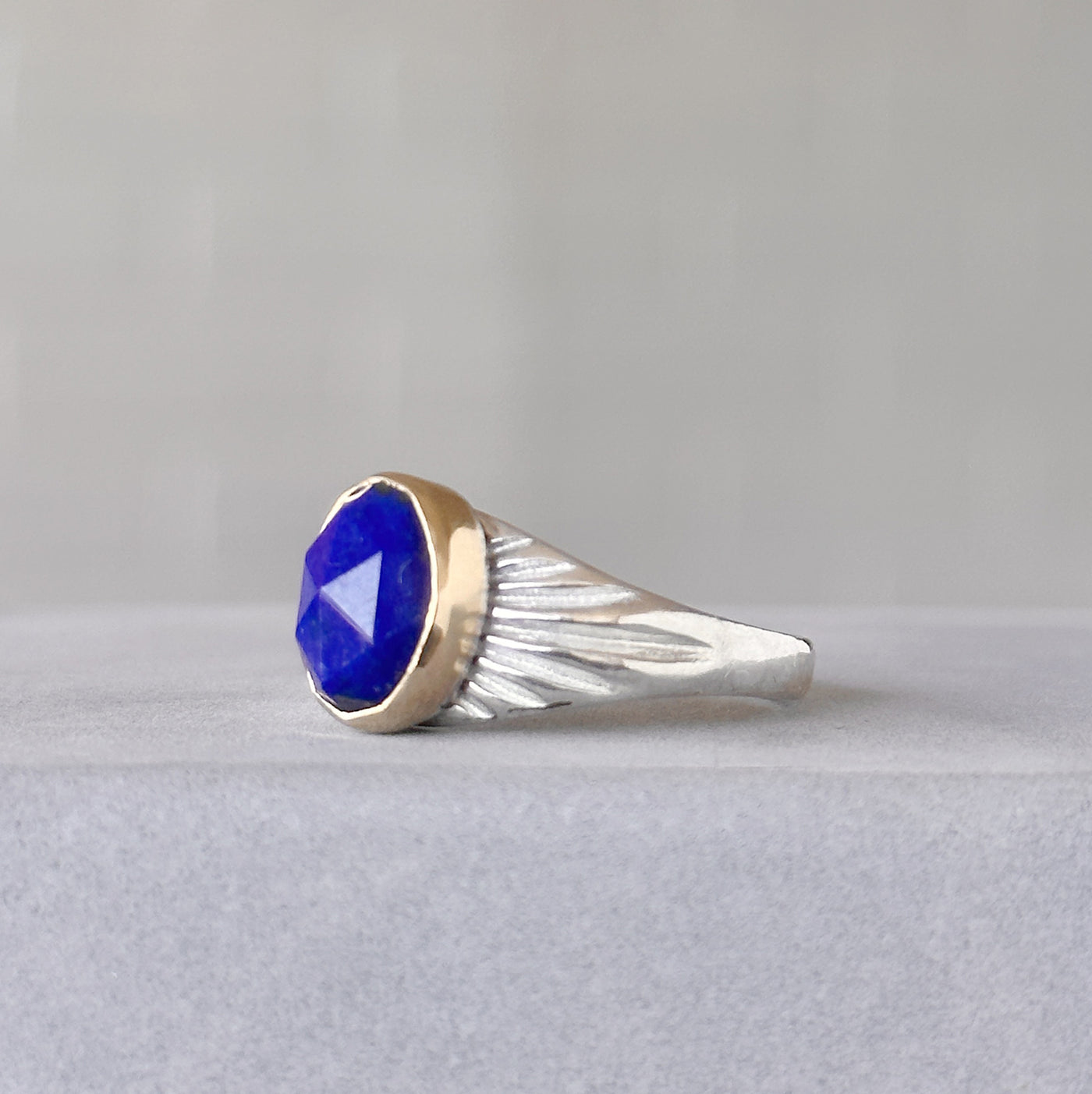 Oval Rose cut Lapis Silver and Gold Sunburst Ring sitting in front of a white wall, side angle