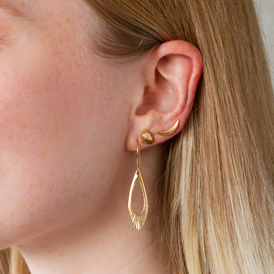 A model's ear wearing a vermeil flux earring, a vermeil and diamond tiny fragment stud, and a vermeil wisp earclimber