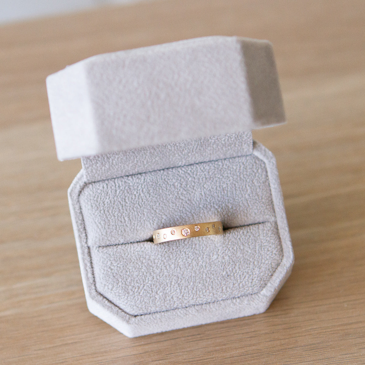 Yellow gold matte texture wide wedding band with scattered flush set diamonds by Corey Egan in a ring box