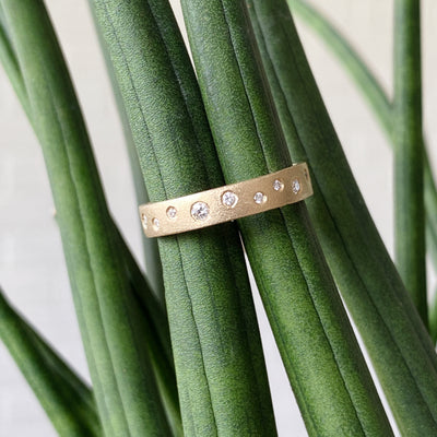 Yellow gold matte texture wide wedding band with scattered flush set diamonds by Corey Egan in natural light