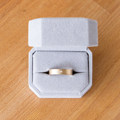 Yellow gold Yosemite flat stippled texture wedding band with a single flush set diamond in a ring box