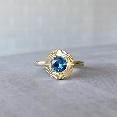 Round Medium Blue Montana sapphire in a 14k yellow gold Aurora ring with an engraved halo border in natural light