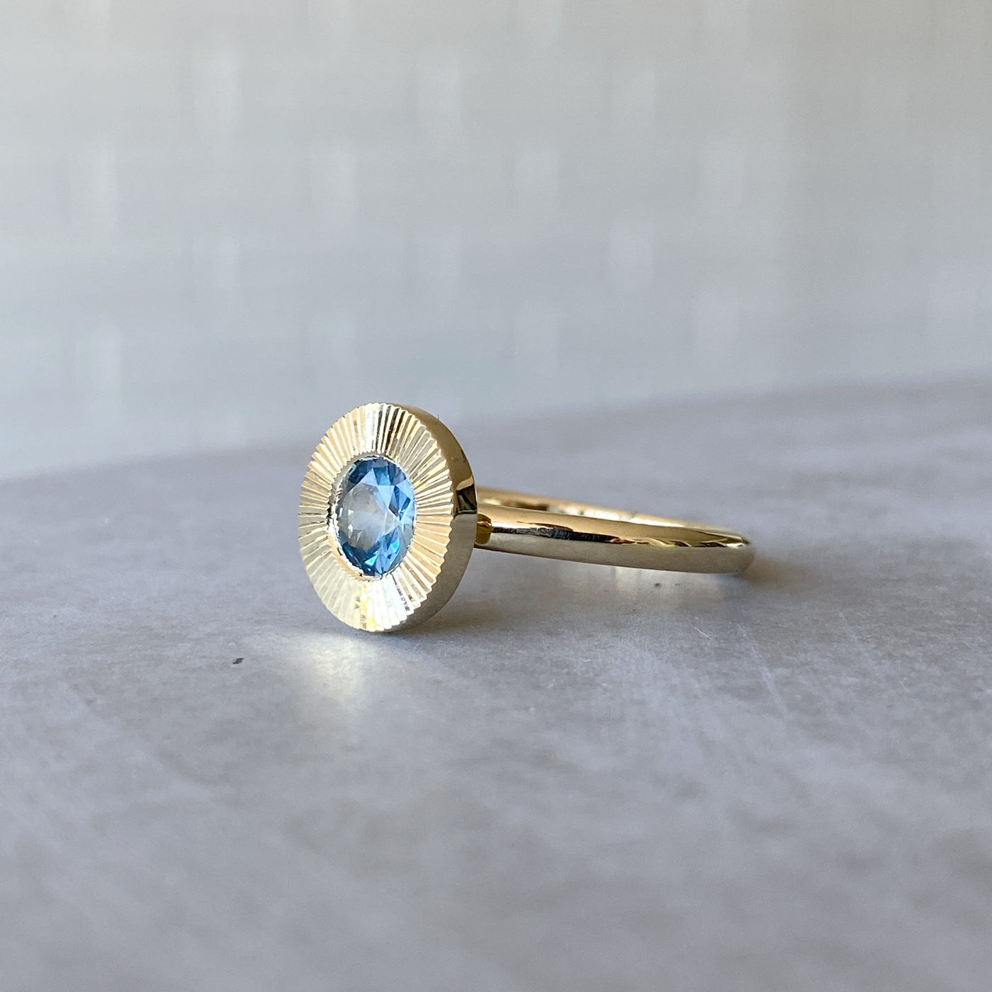 Side view of round Medium Blue Montana sapphire in a 14k yellow gold Aurora ring with an engraved halo border in natural light.