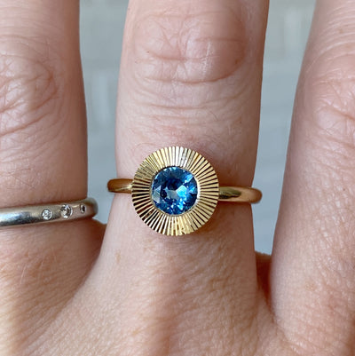 Round Medium Blue Montana sapphire in a 14k yellow gold Aurora ring with an engraved halo border on a hand
