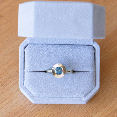 Round Teal Montana sapphire in a 14k yellow gold Aurora ring with an engraved halo border in a ring box