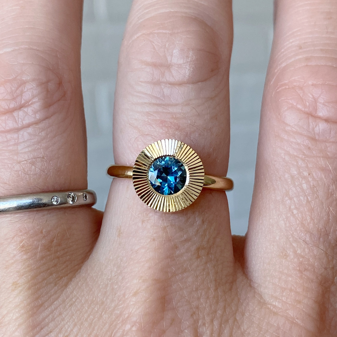 Round Teal Montana sapphire in a 14k yellow gold Aurora ring with an engraved halo border on a hand