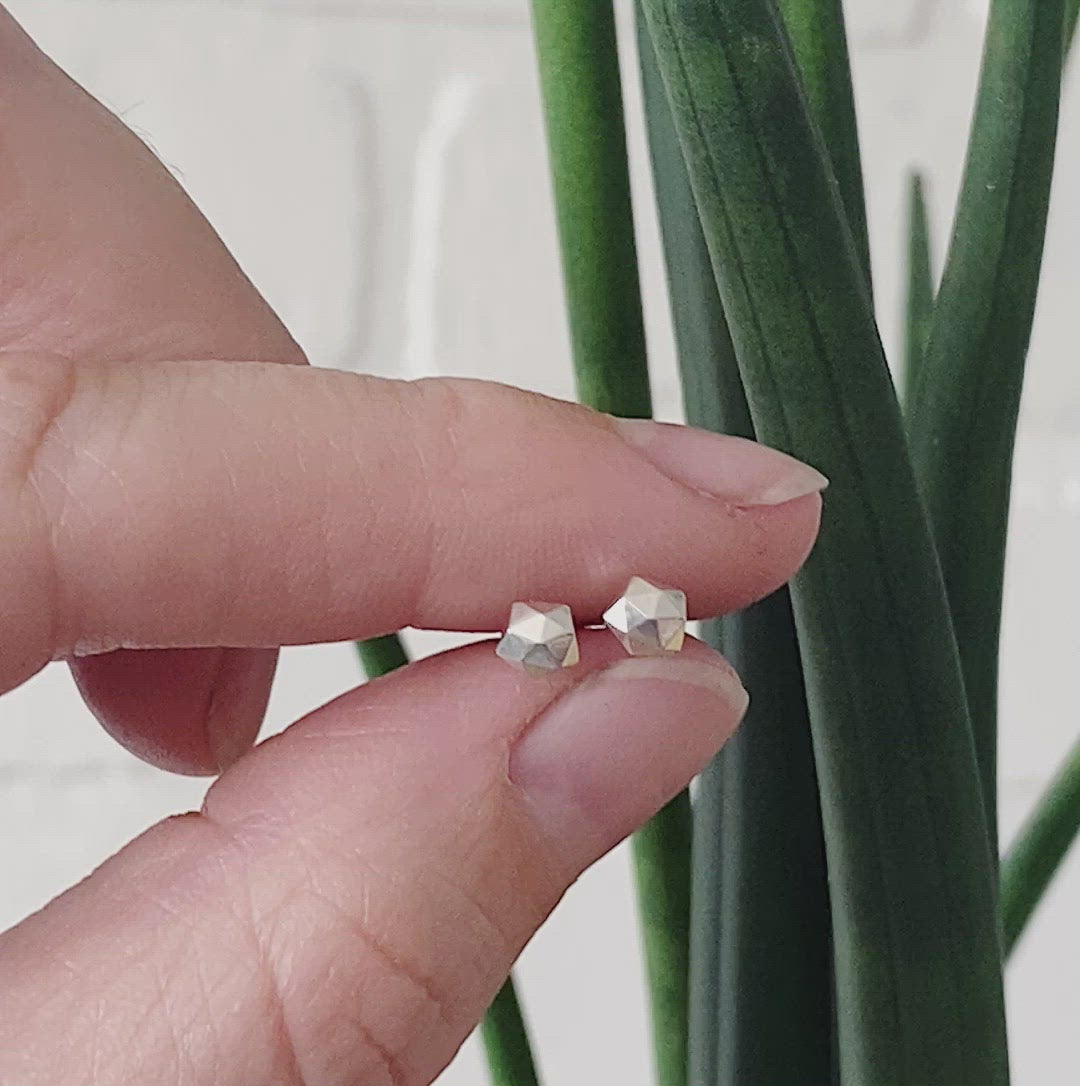 sterling silver micro size geometric faceted stud earrings by Corey Egan between two fingers for scale