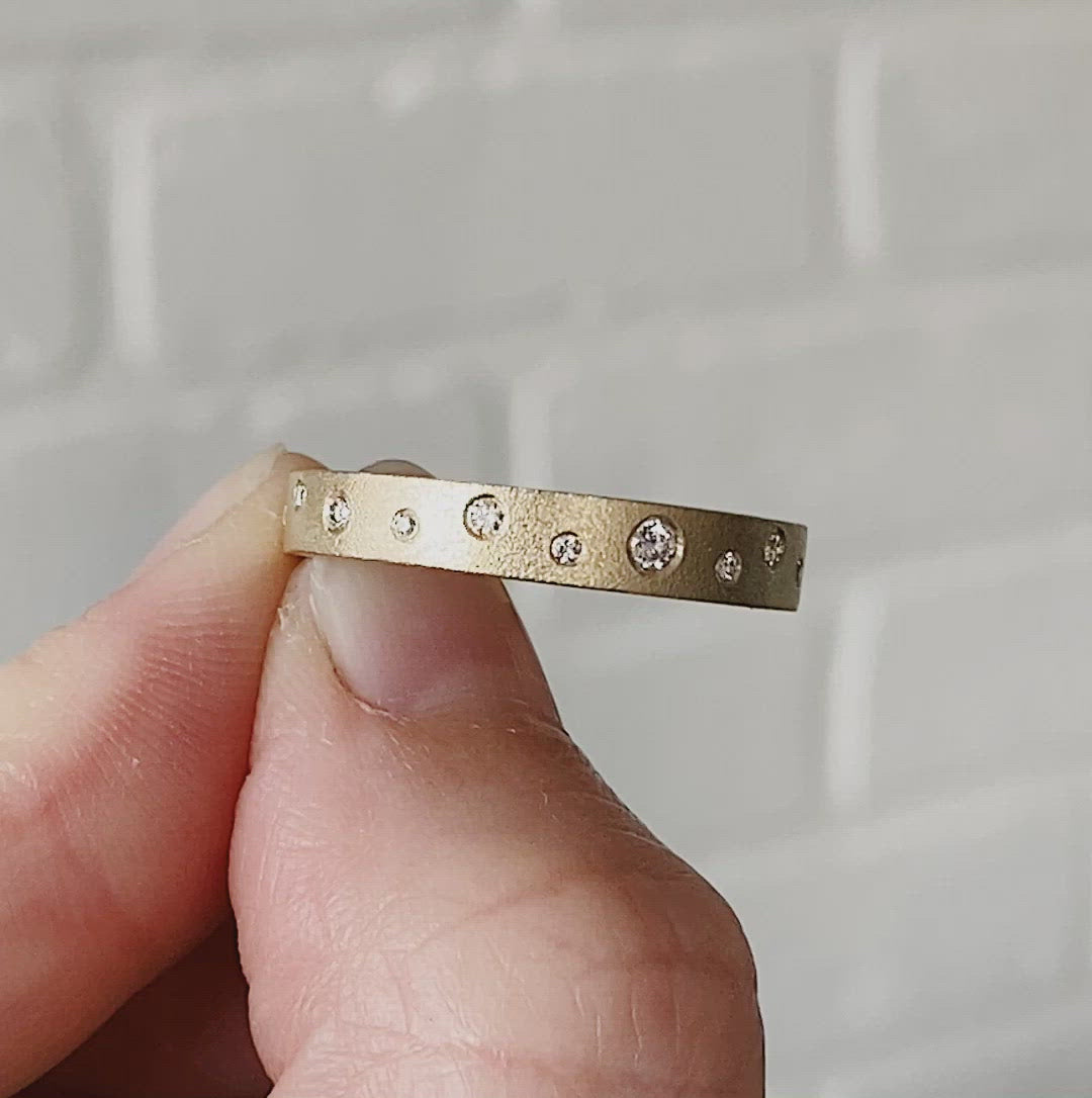Yellow gold matte texture wide wedding band with scattered flush set diamonds by Corey Egan being rotated around in a pair of fingers