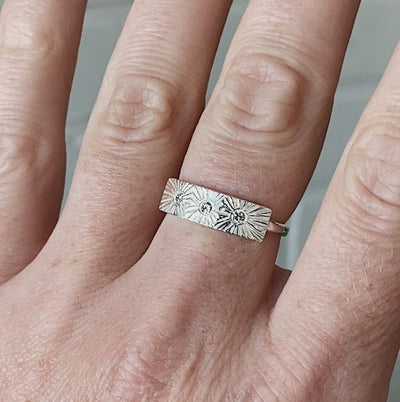 Sterling silver bar ring with three diamonds and a carved sunburst design around each by Corey Egan on a hand