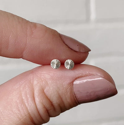 Tiny engraved silver stud earring by Corey Egan between two fingers