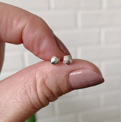 sterling silver micro size geometric faceted stud earrings with a single flush set diamond by Corey Egan between two fingers for scale