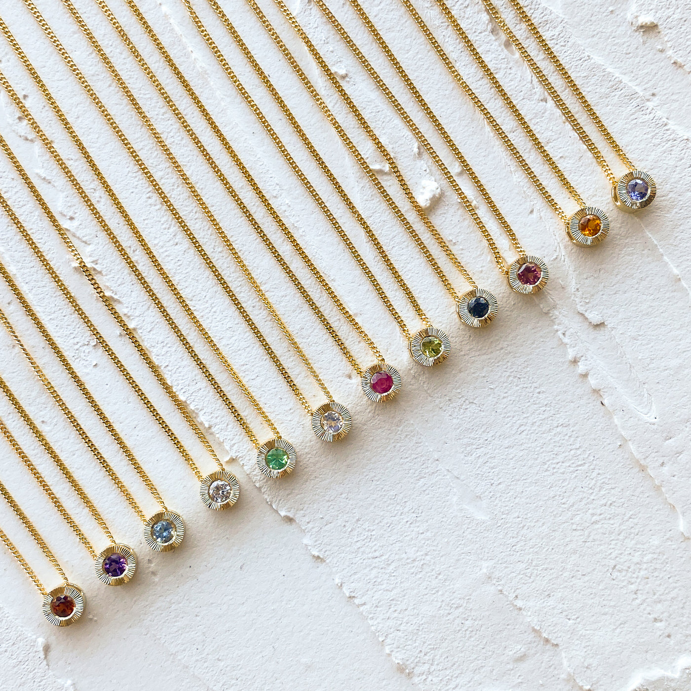 Birthstone Aurora necklaces in 14k yellow gold in each birthstone: garnet for January, amethyst for February, aquamarine for March, diamond for April, emerald for May, moonstone for June, ruby for July, peridot for August, blue sapphire for September, pink tourmaline for October, citrine for November, and tanzanite for December